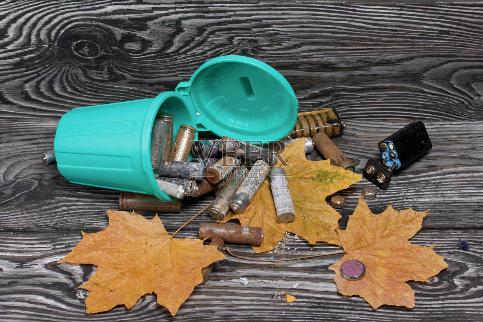 腐蚀电池使用。他们躺在一个翻倒的垃圾桶里和周围。干枫叶就在附近。处置危险废物。照片摄影图片