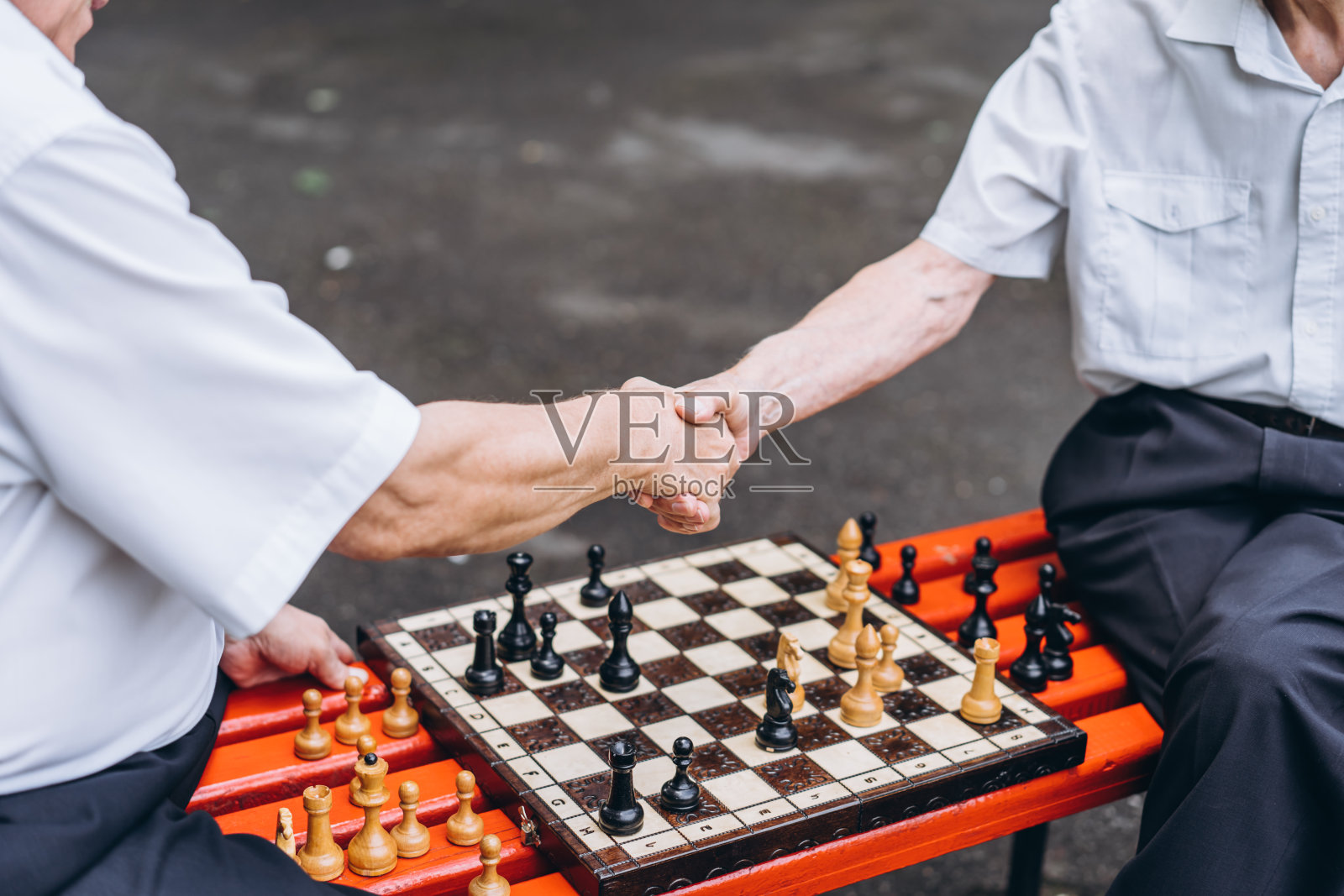 两个年长的男人在公园外面的长椅上下棋。照片摄影图片