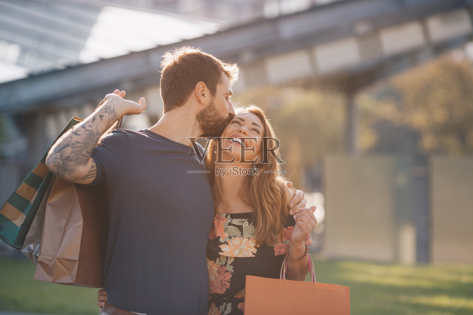 一对热恋中的年轻情侣购物归来，手里提着购物袋，丈夫吻了妻子照片摄影图片