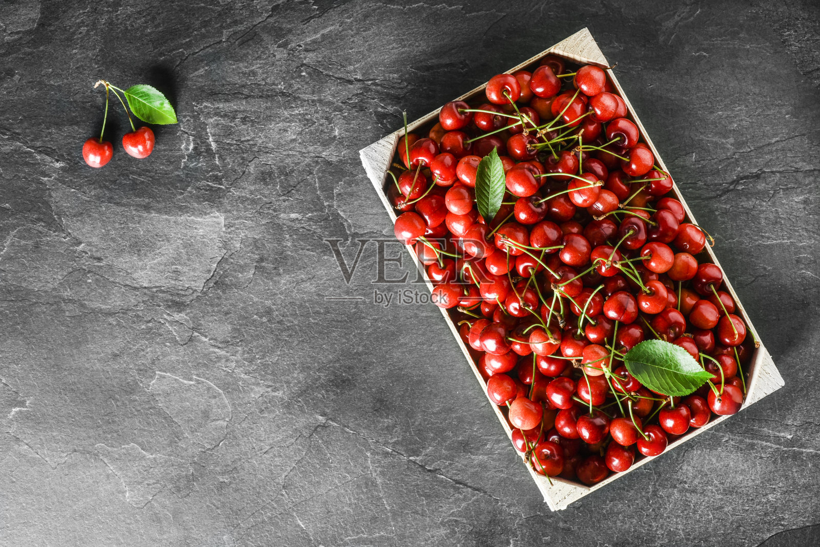 俯视图樱桃在深色的石头桌子与树叶。照片摄影图片