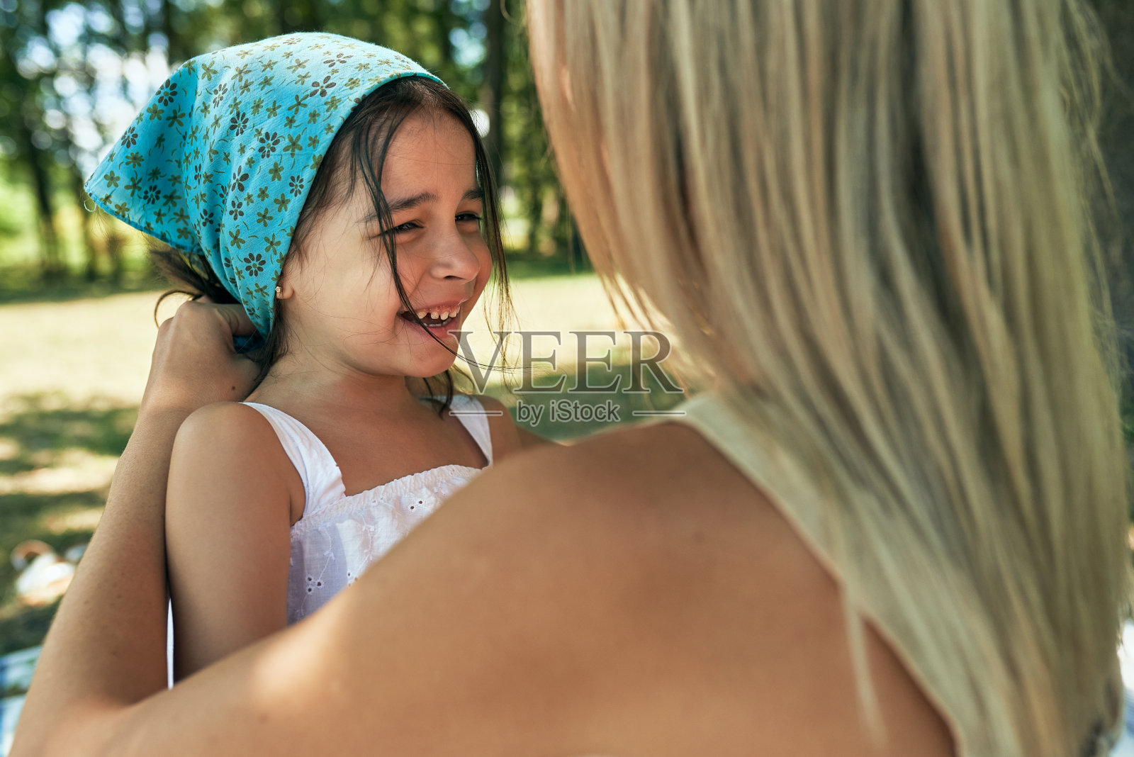 在阳光明媚的夏日里，快乐的女儿和妈妈在公园里玩耍的特写。女人和孩子在户外惬意的野餐。在外面，妈妈在孩子头上系了一条围巾。母亲节照片摄影图片