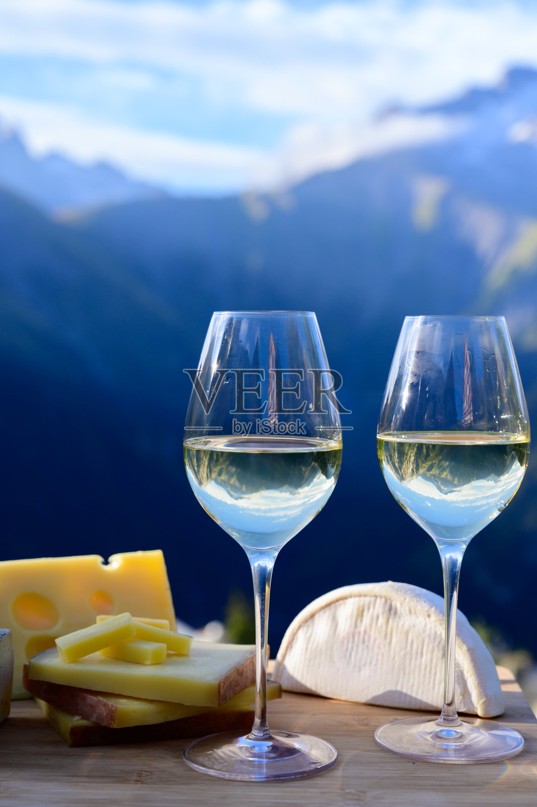 来自法国萨沃伊地区的美味奶酪和葡萄酒，beaufort, abondance, emmental, tomme和reblochon de savoie奶酪和一杯白葡萄酒，以阿尔卑斯山的山峰为背景照片摄影图片