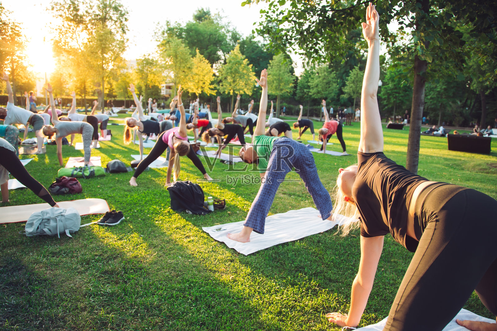 日落时分，一群年轻人在公园里做瑜伽。照片摄影图片