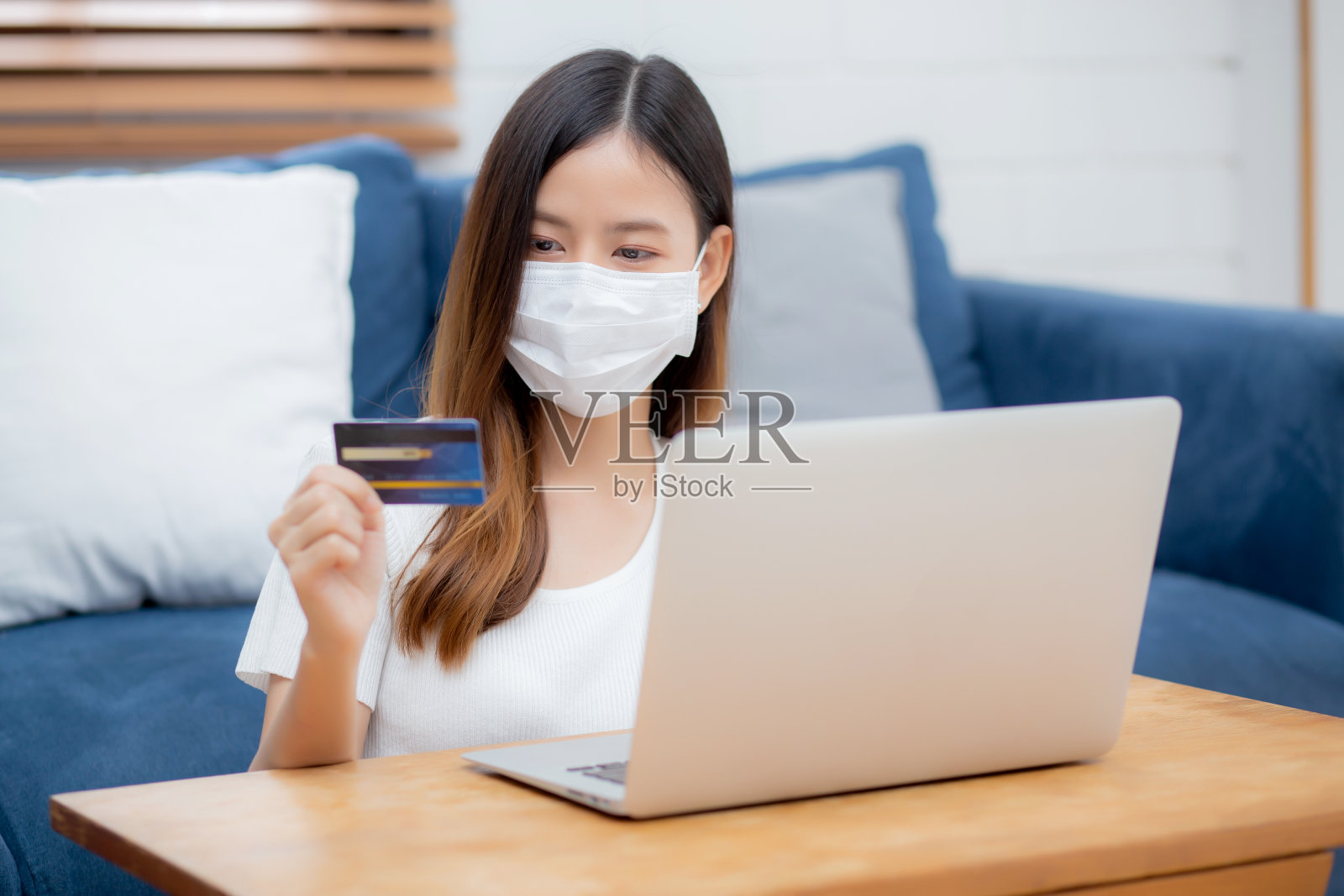 年轻的亚洲女子戴着面具用信用卡在网上购物用笔记本电脑购买和支付，女孩用借记卡购买或交易金融，生活方式和新常态的概念。照片摄影图片