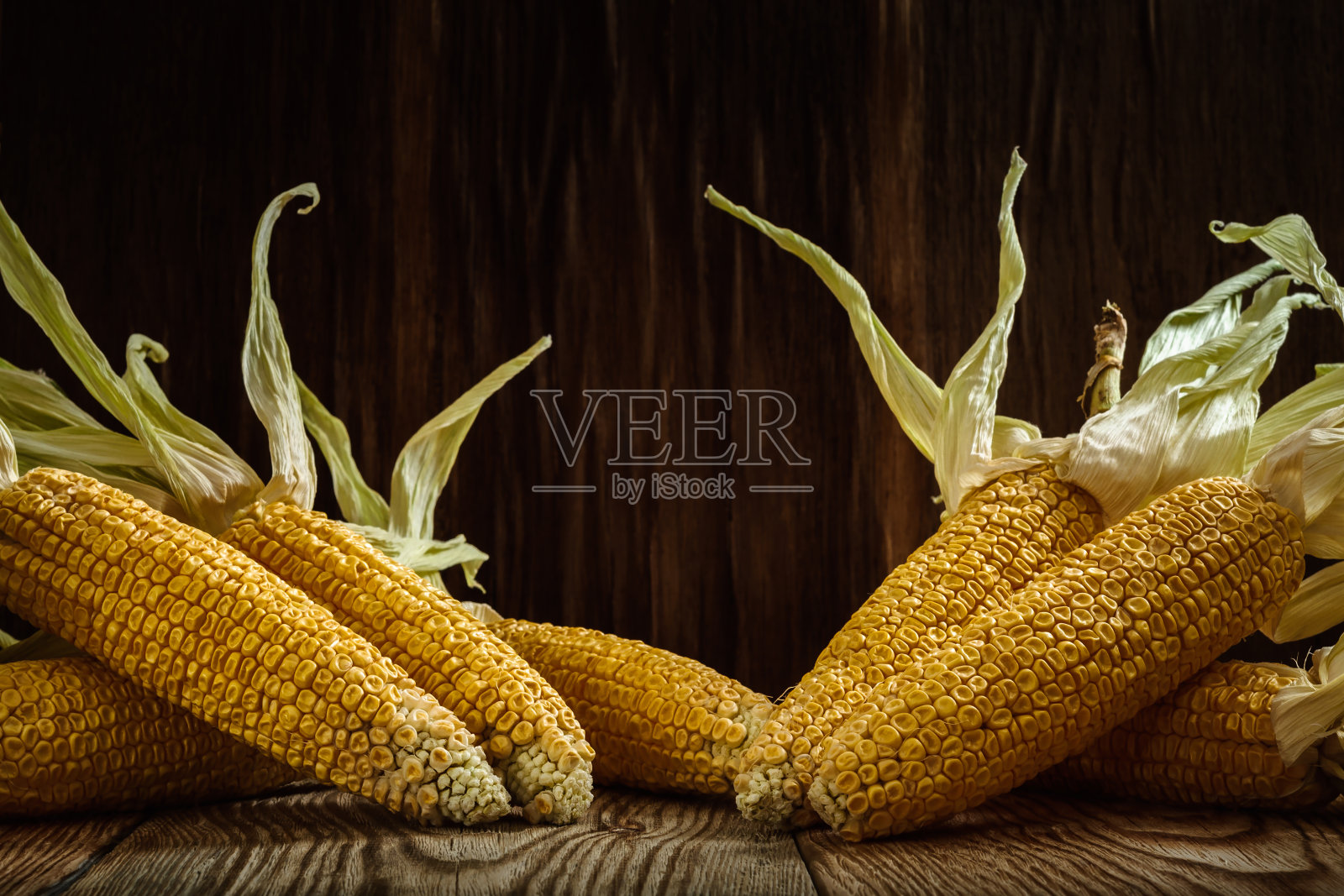 在深色木质背景下，在粗糙的木板上放置带壳的干玉米棒。四季秋朴的概念照片摄影图片