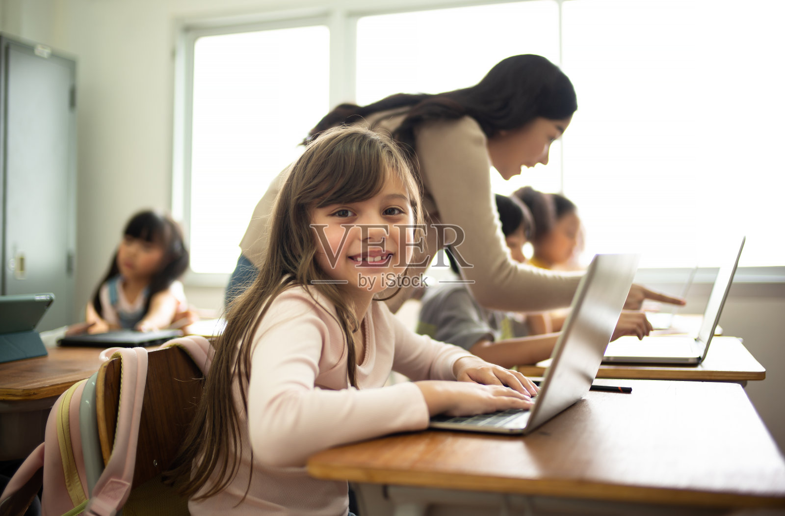 小学计算机课上小女孩对着相机微笑的肖像。教育、学校、技术和互联网的概念。照片摄影图片