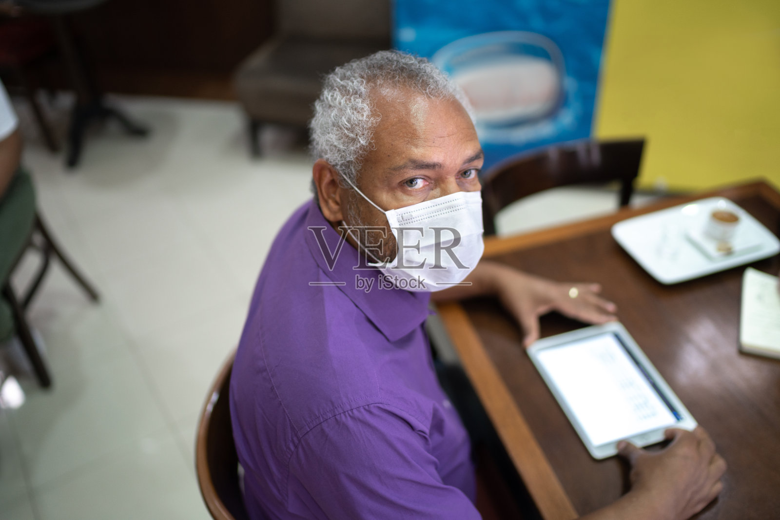 一个成年男子戴着口罩在咖啡店里使用平板电脑的肖像照片摄影图片