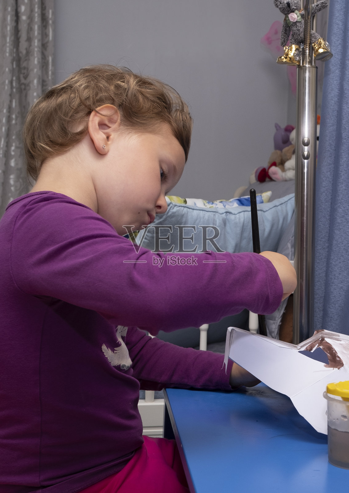 一名5岁的白人女孩坐在桌旁，用水彩颜料绘制纸面具照片摄影图片