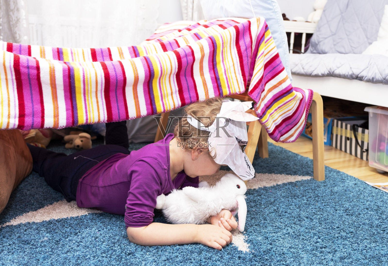 一个小孩，一个5岁的女孩，扮演一只狼。孩子的头上戴着一个纸狼面具。那孩子用毛巾和椅子给自己盖了个洞。照片摄影图片