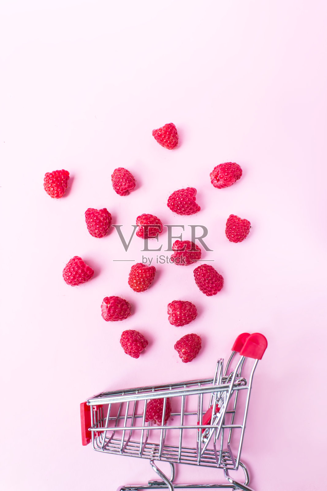 粉红色背景上的覆盆子落在购物车里。健康膳食购物，丰富和幸福的概念。照片摄影图片
