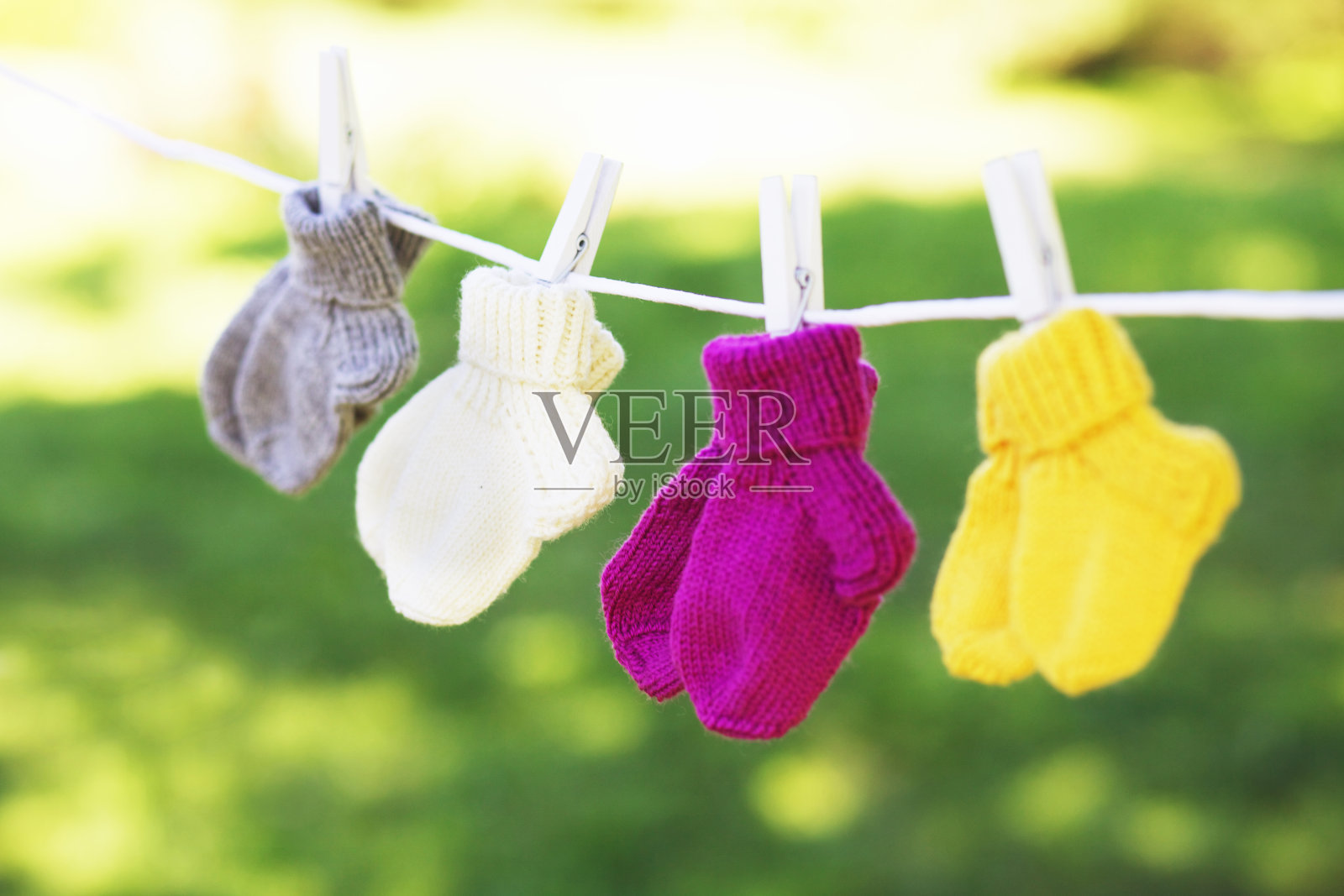 近距离的羊毛袜-儿童尺寸-挂在绳子上在阳光下晾干-粉红色，黄色，白色，灰色-可爱的手工婴儿袜。照片摄影图片