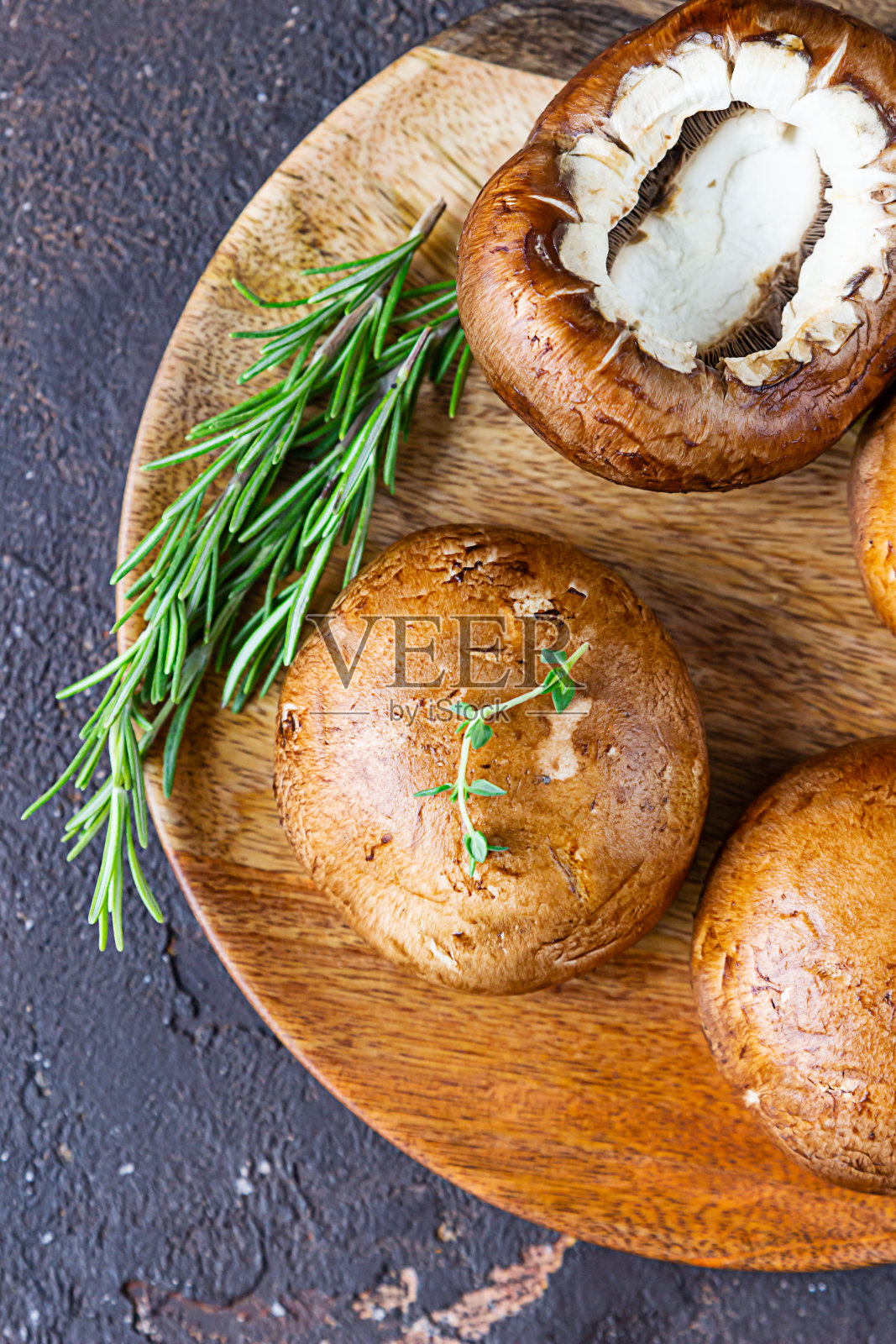 新鲜美味的波多贝罗蘑菇配百里香和迷迭香在木切板上，黑色的石头背景。前视图。照片摄影图片