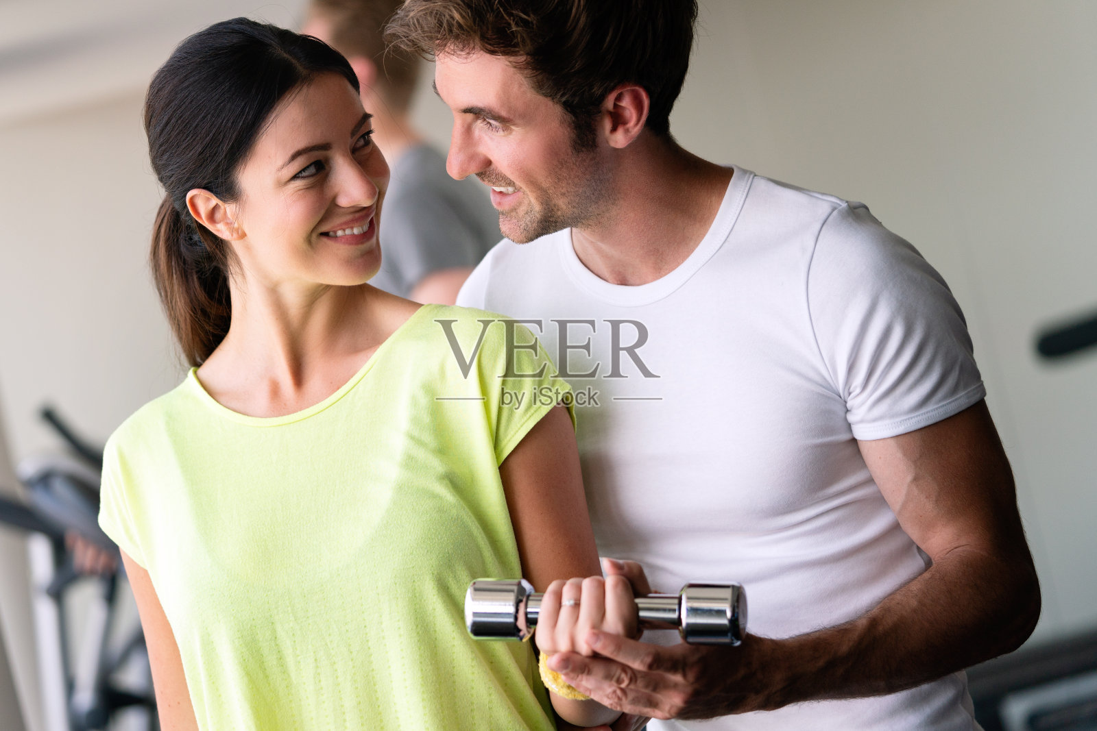 男子教练调情与美丽的年轻女子，同时帮助她在健身房照片摄影图片