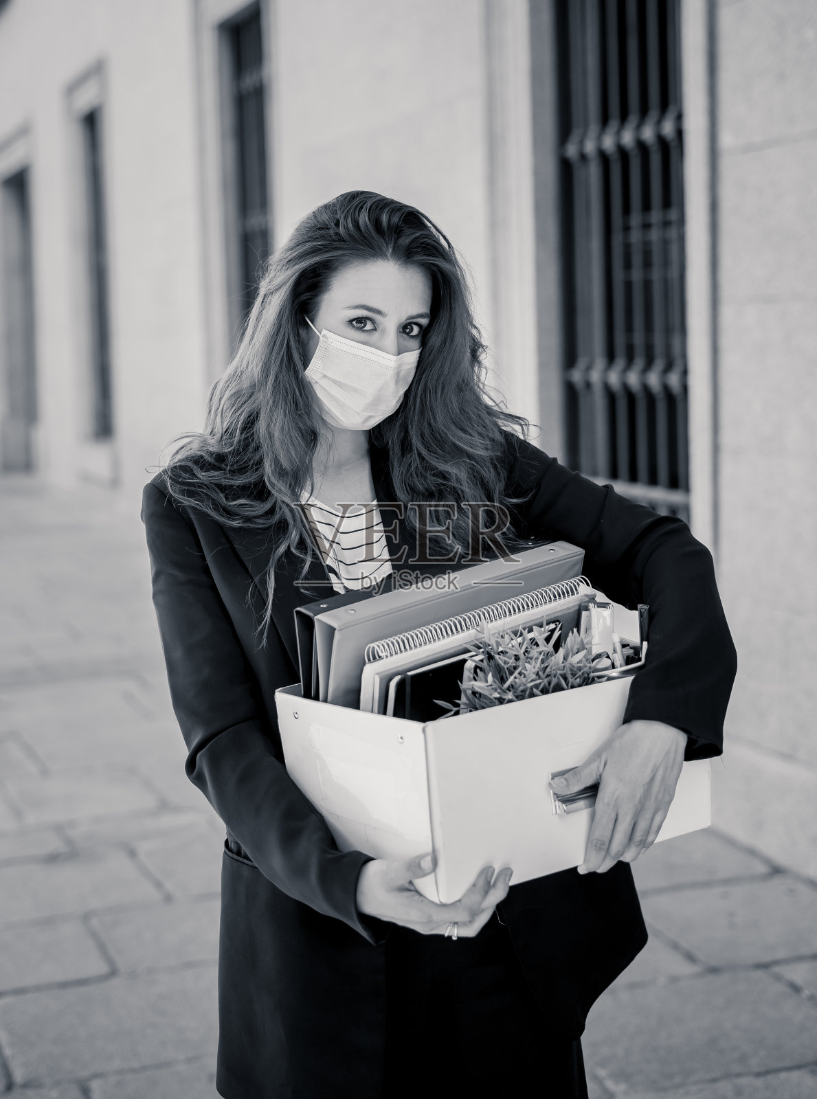 在商业区戴着医用防护口罩的悲伤女商人，办公室职员因失业而感到沮丧。新冠病毒裁员、COVID-19失业和经济危机概念。照片摄影图片