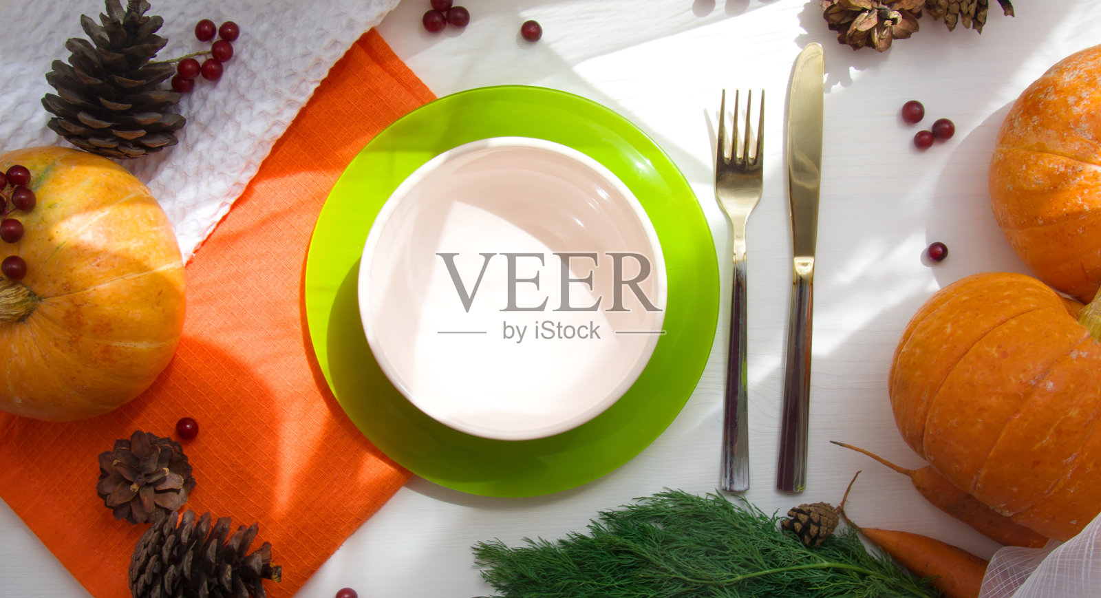 白色的木制餐桌上放着南瓜、胡萝卜、欧芹和蛋卷，旁边放着橙色的餐巾，阳光下放着一个空盘子。秋天的收获。万圣节。从以上观点。照片摄影图片