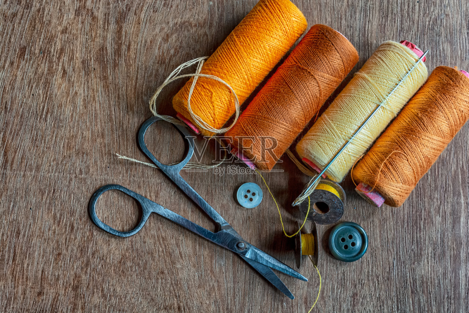 四种不同色调的黄色和棕色的缝纫线轴与针和缝纫配件在棕色的木制背景。照片摄影图片