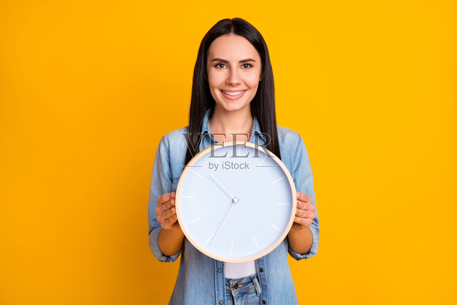 她的肖像，她好看，迷人，可爱，迷人，开朗，快乐的女孩手牵着显示圆形的脸时钟孤立在明亮，生动的明亮，明亮的黄色背景照片摄影图片