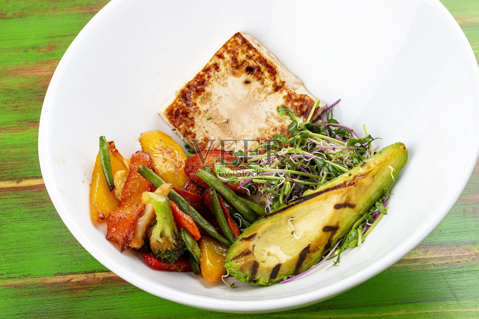 炒豆腐配烤牛油果和炒菜。在一个彩色的木制背景上。素食菜。照片摄影图片