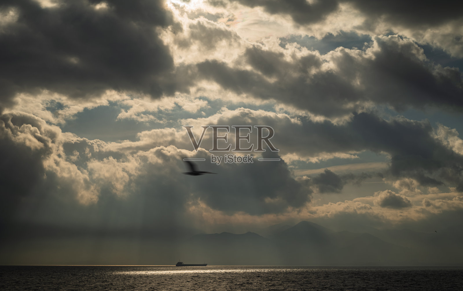 透过云层的日光和大海中央的油轮照片摄影图片