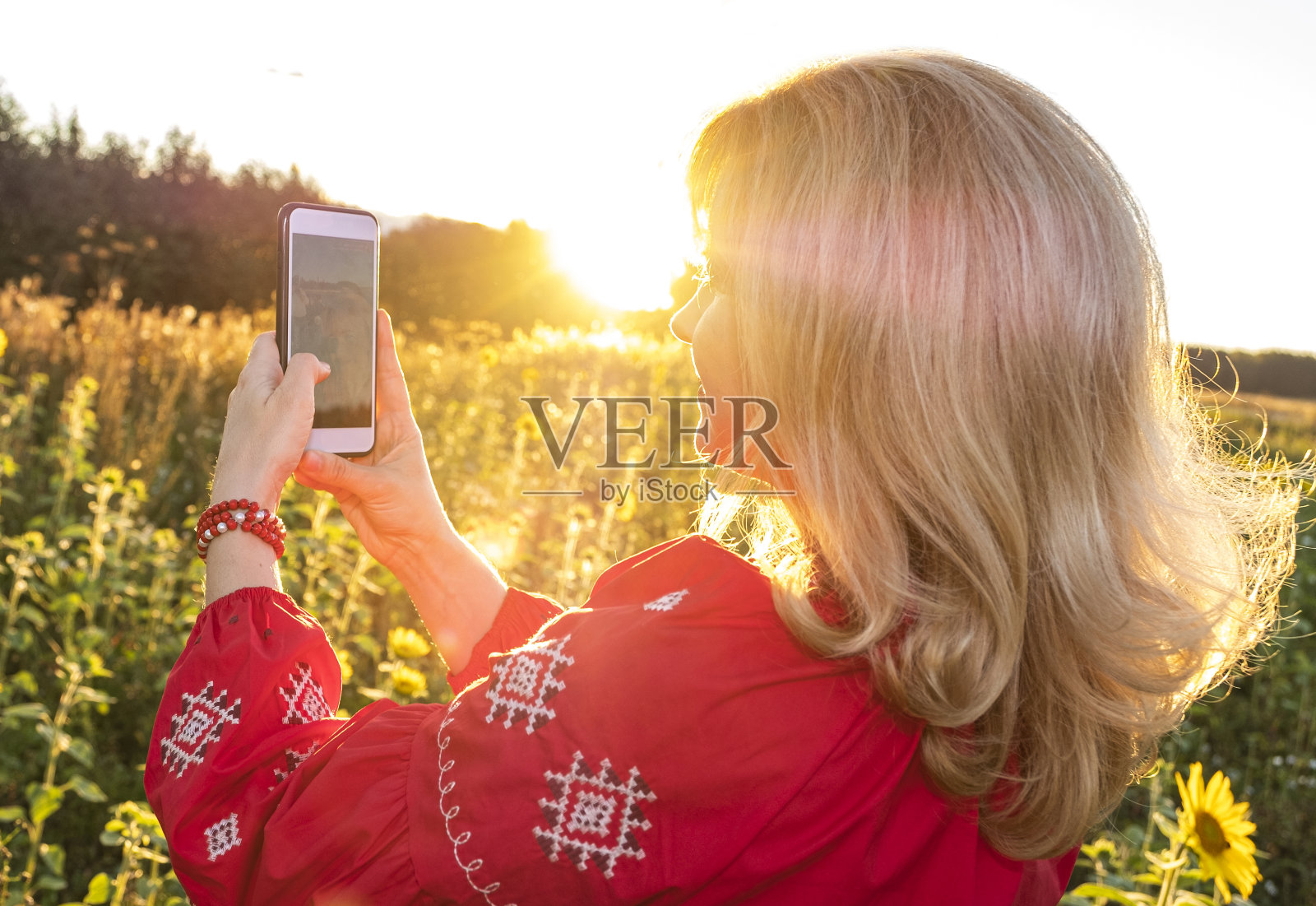 穿着红色衣服的年轻白人女人。在日落的背景下自拍。乡间的向日葵田。照片摄影图片