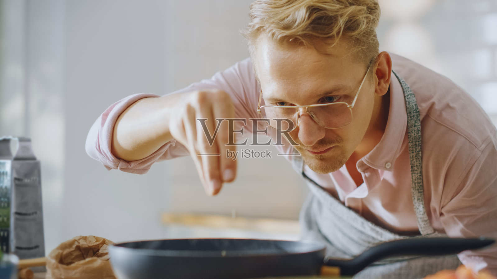 英俊的年轻人在煎锅上准备健康的素食。在现代厨房里洒上健康的绿色食物和香料。自然清洁饮食与健康生活理念。照片摄影图片