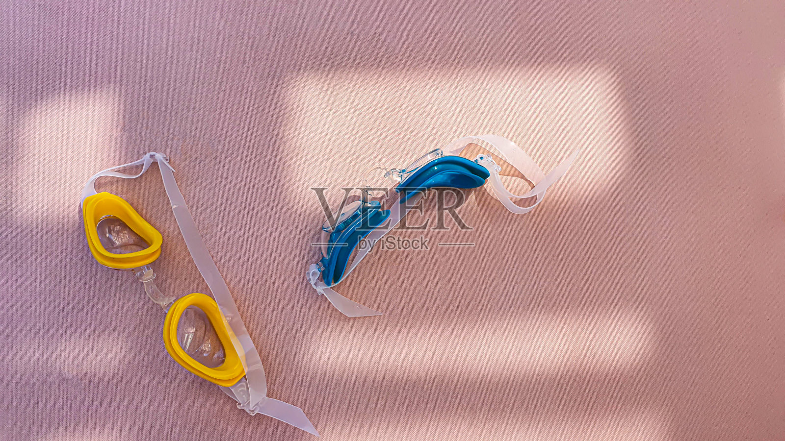 在游泳池附近的高架床上游泳的儿童护目镜。黄色和蓝色。太阳光造成一幅阴影图。照片摄影图片