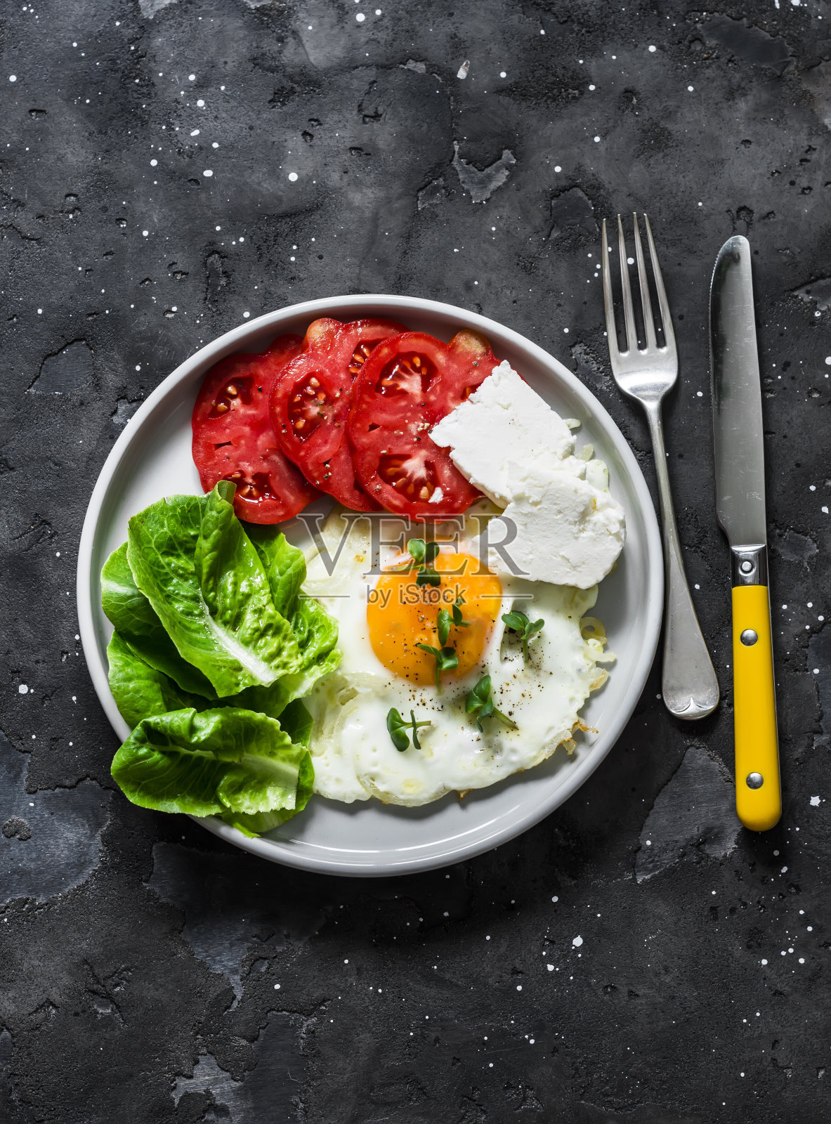 美味的早餐，小吃，小吃-煎蛋，成熟的西红柿，希腊奶酪，绿色沙拉在一个黑暗的背景，俯视图照片摄影图片