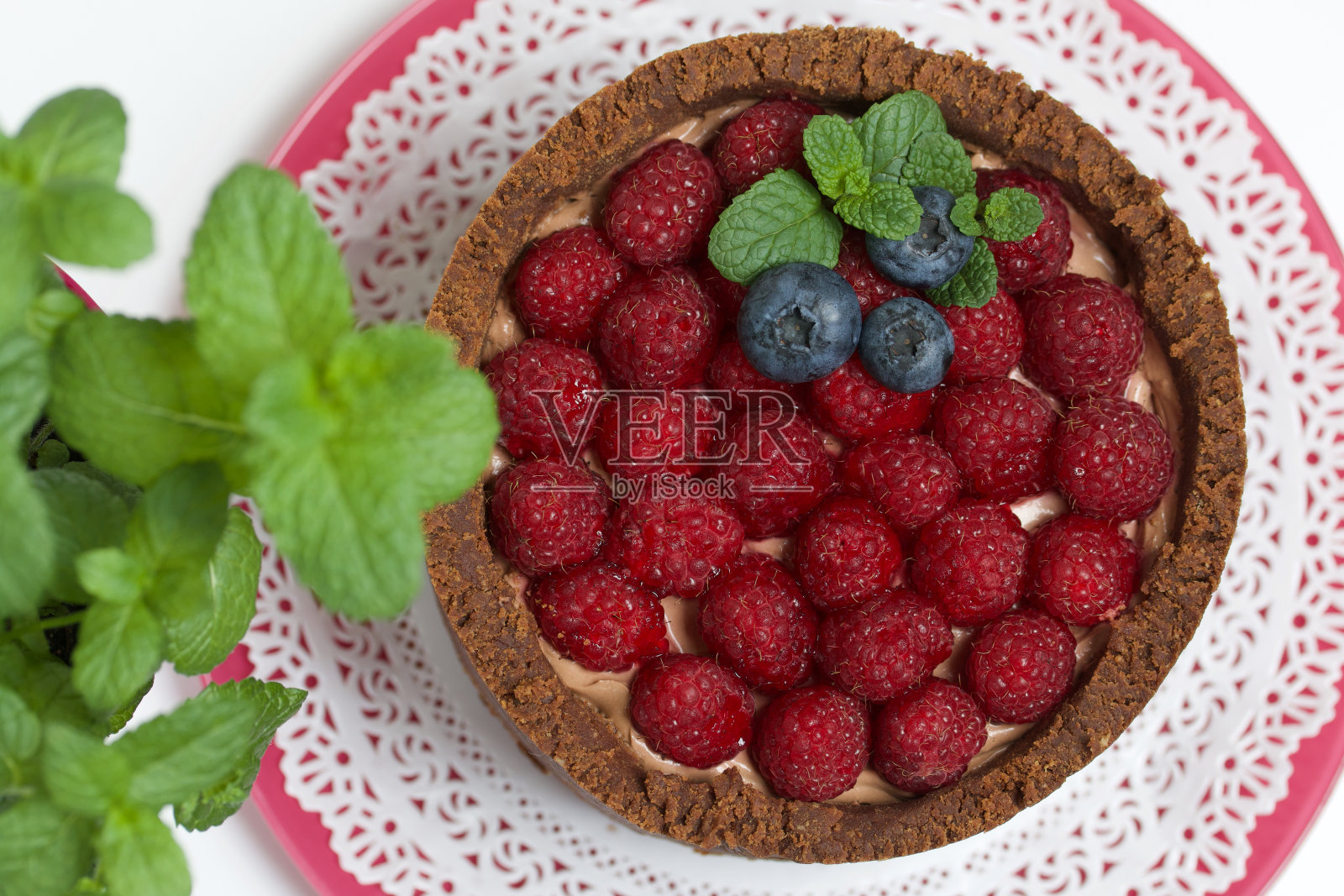 不烤奶油芝士巧克力蛋糕。装饰有覆盆子、蓝莓和薄荷叶。附近有一罐薄荷。在白色的表面上。照片摄影图片