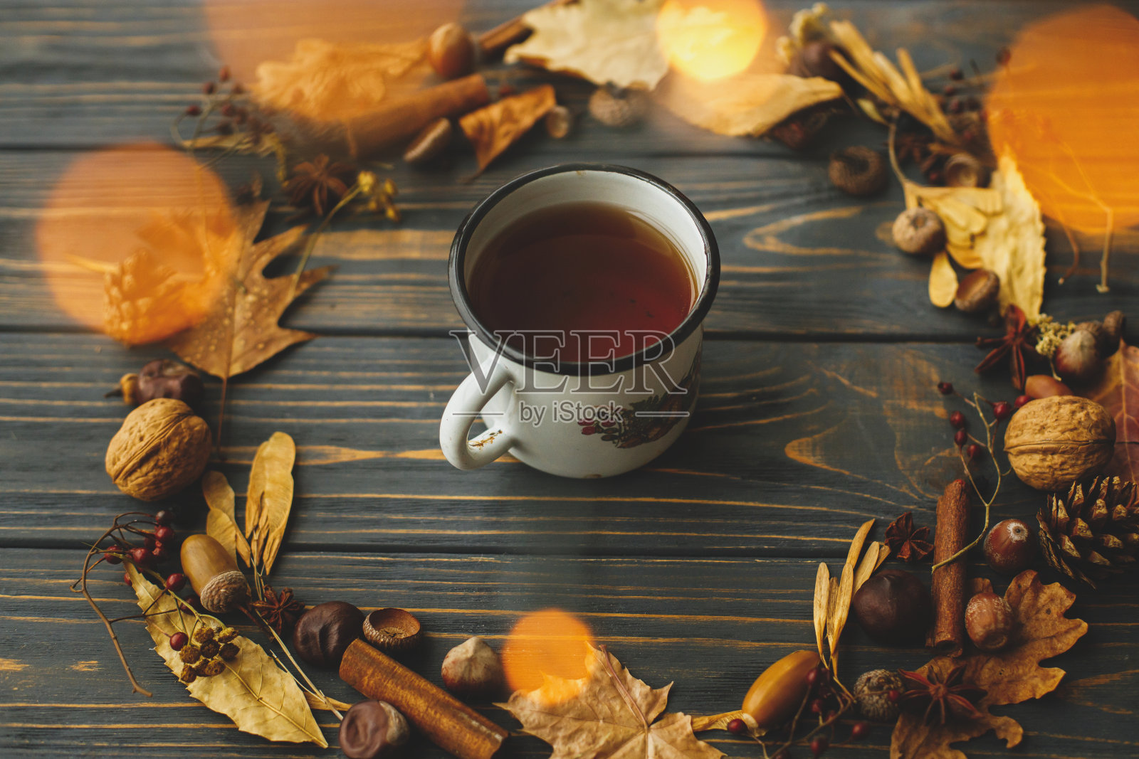 你好下降!乡村的秋天的形象。复古金属杯，茶和秋季花环由树叶，浆果，橡子和松果在深色的木质背景和温暖的灯光。照片摄影图片