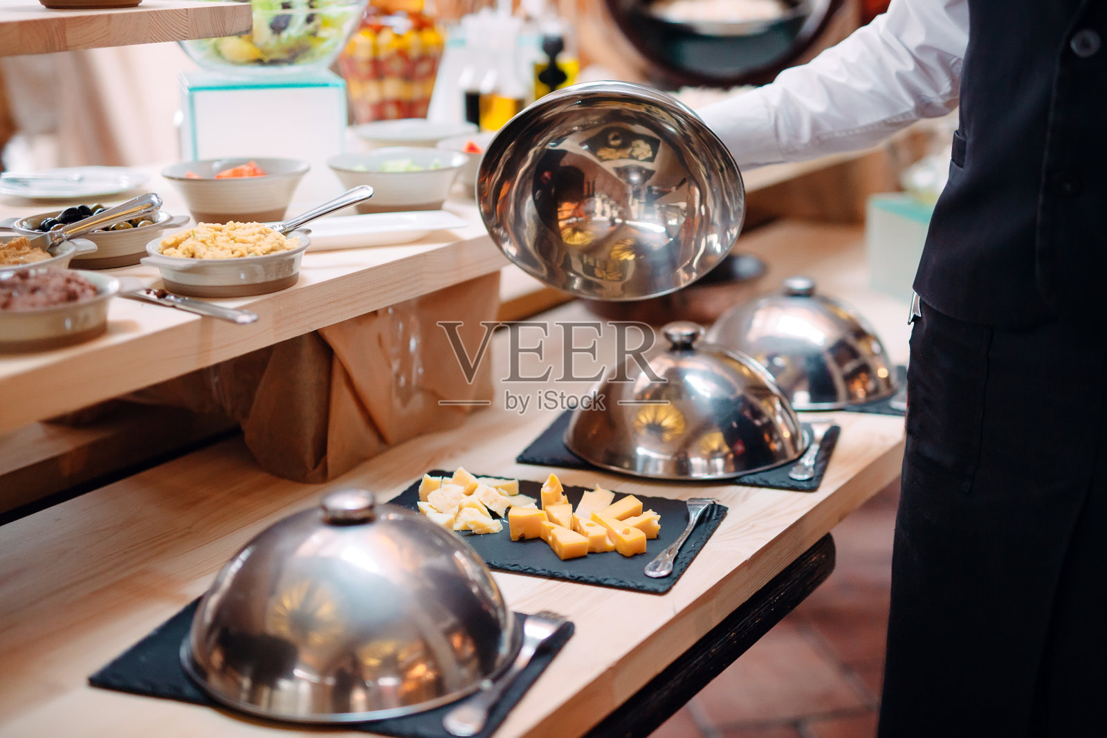 在带帽的金属碗上切奶酪。酒店或餐厅早餐。照片摄影图片