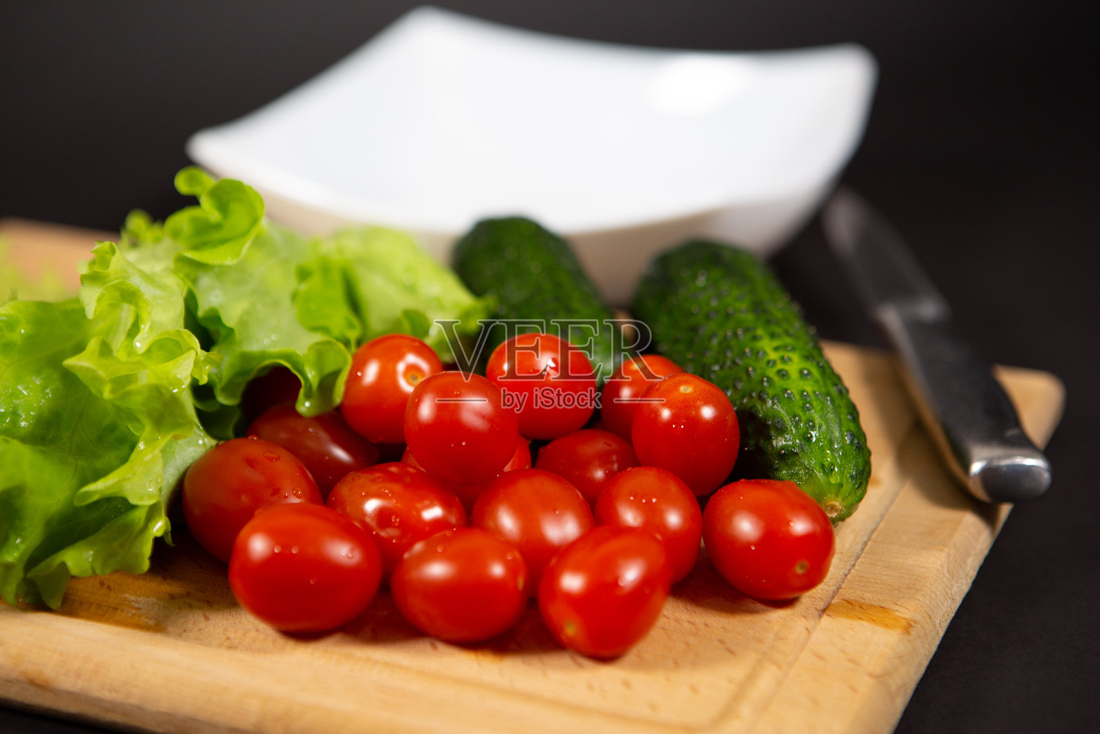 将新鲜多汁的圣女果、黄瓜、小黄瓜和莴苣叶用水滴放在木砧板上。农民送来的新鲜蔬菜。照片摄影图片