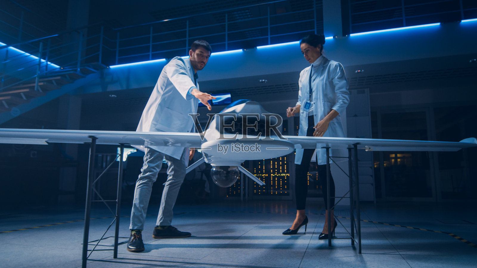 从事无人机/无人机原型研究的航天工程师会议。穿着白大褂的航空科学家在说话。工业实验室商用空中侦察飞机照片摄影图片