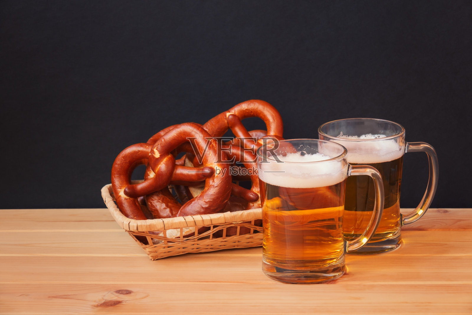 深色背景的木桌上放着两个啤酒杯和柳条篮子，上面放着柔软的椒盐卷饼。有选择性的重点。照片摄影图片