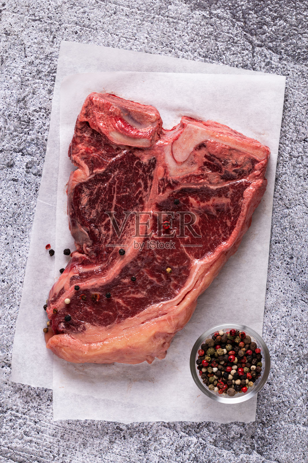 新鲜生t骨牛排在灰色的石头背景。照片摄影图片