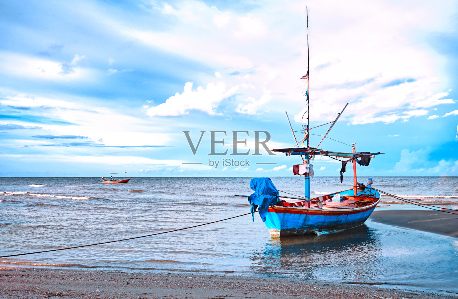 在美丽的蓝天背景下，落潮后的蓝色小渔船停泊在海滩上。照片摄影图片