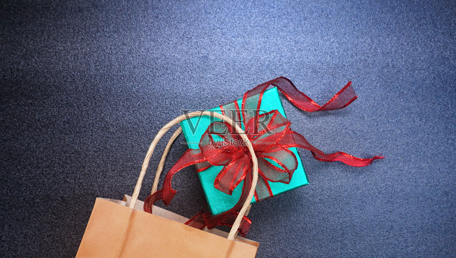 顶角视图绿色闪光礼盒与红色丝带溢出购物袋在黑色的桌子上照片摄影图片