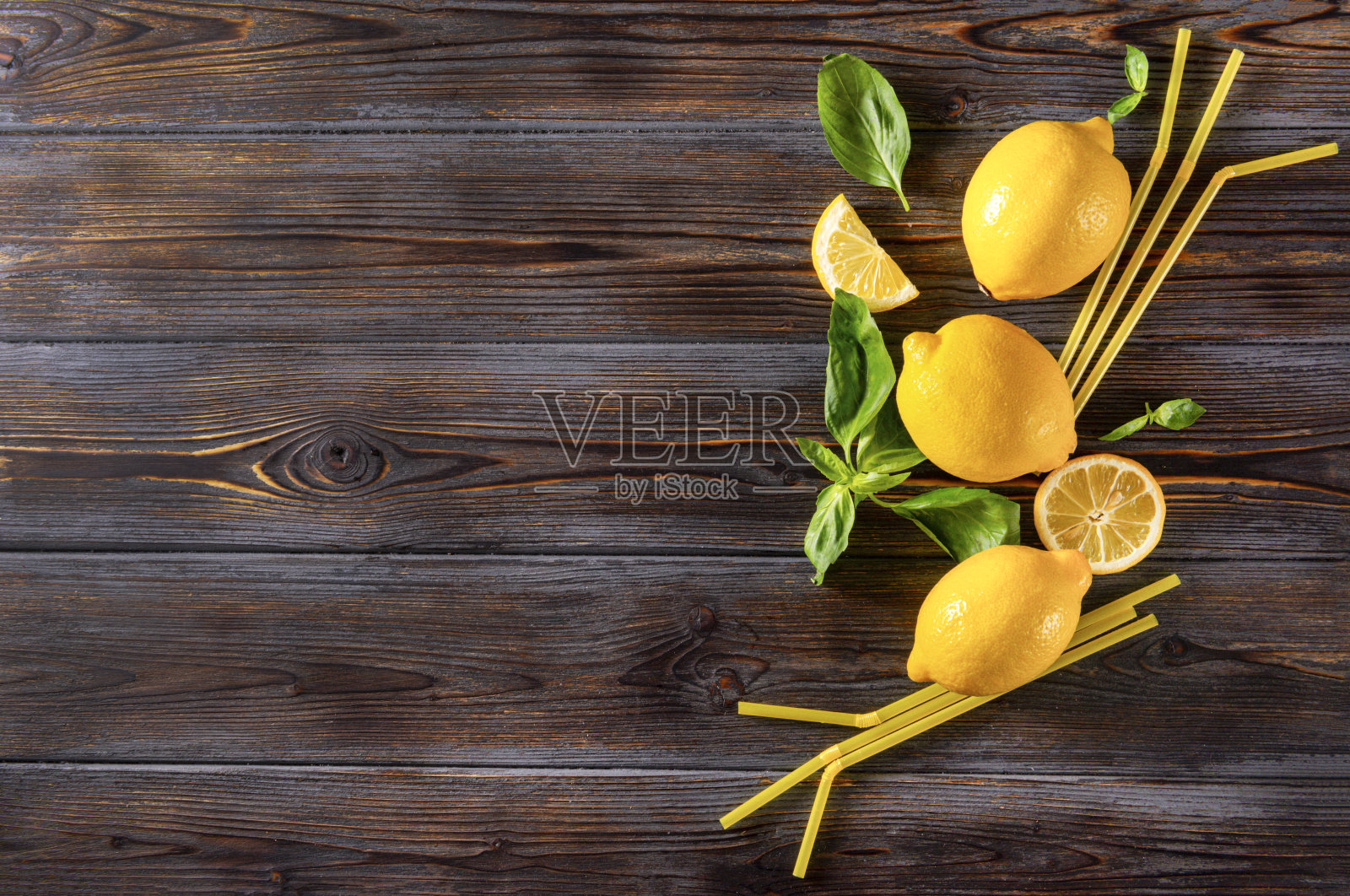 几个黄色的完整柠檬和切片，绿色罗勒的小枝，黄色的管放在深色的木头背景上照片摄影图片