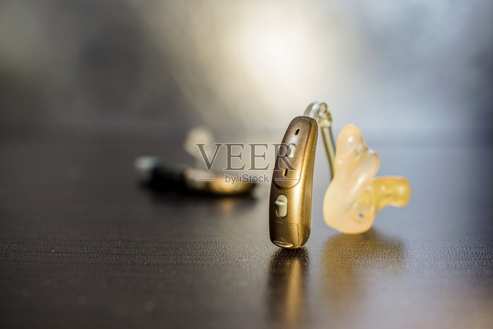 棕色木桌上放着助听器。左耳和右耳使用的电子设备。重点是在前面。照片摄影图片