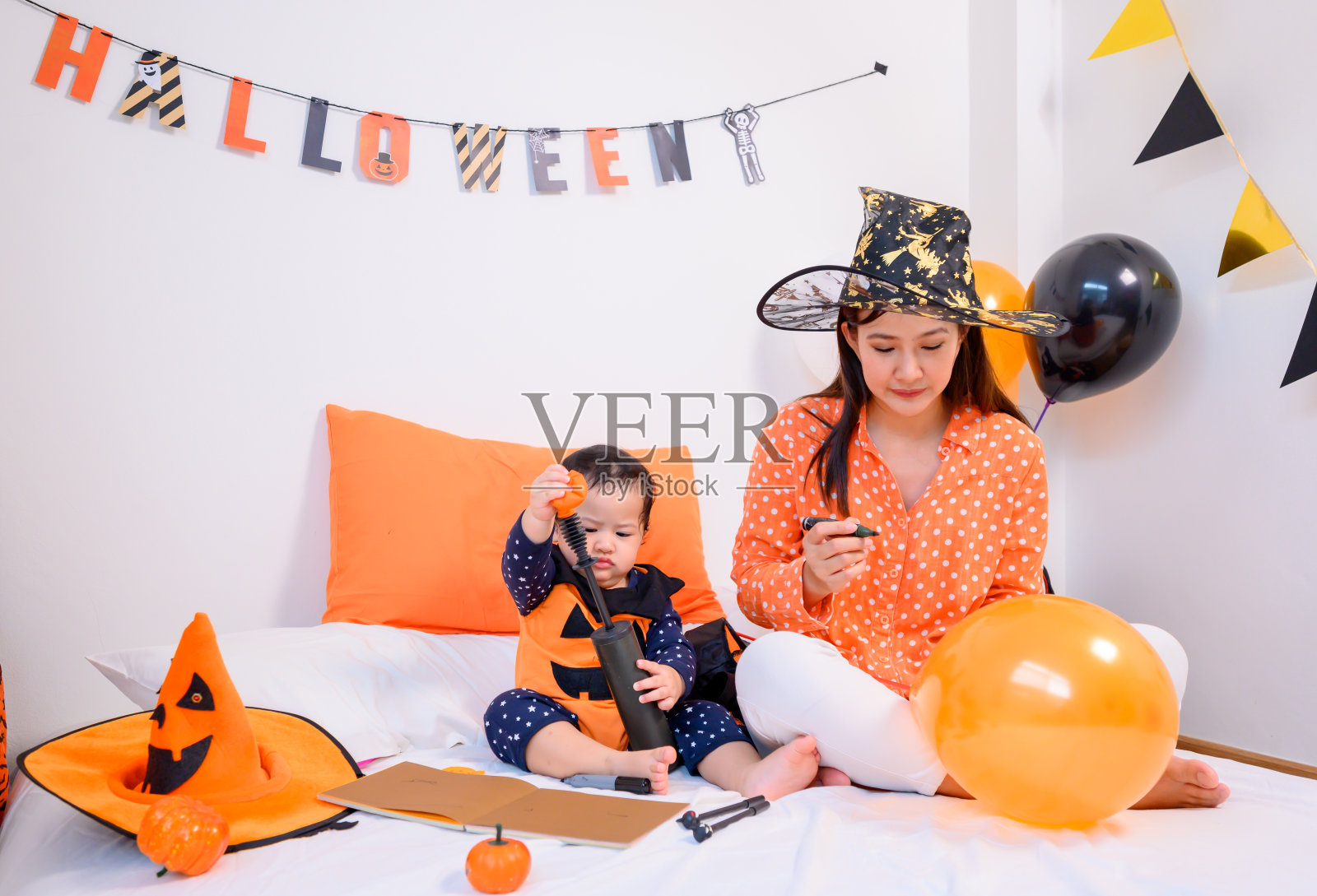 母亲和女儿穿着万圣节服装在家庆祝。孩子和妈妈在卧室装饰秋天的季节。照片摄影图片