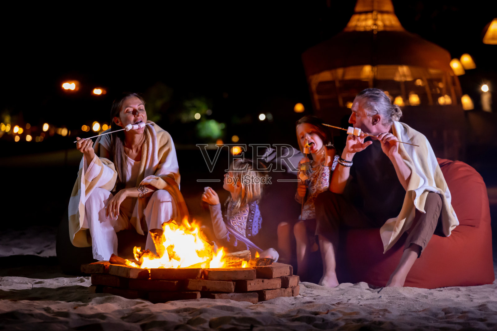 快乐的家庭在海滩露营围坐在篝火旁烤棉花糖照片摄影图片