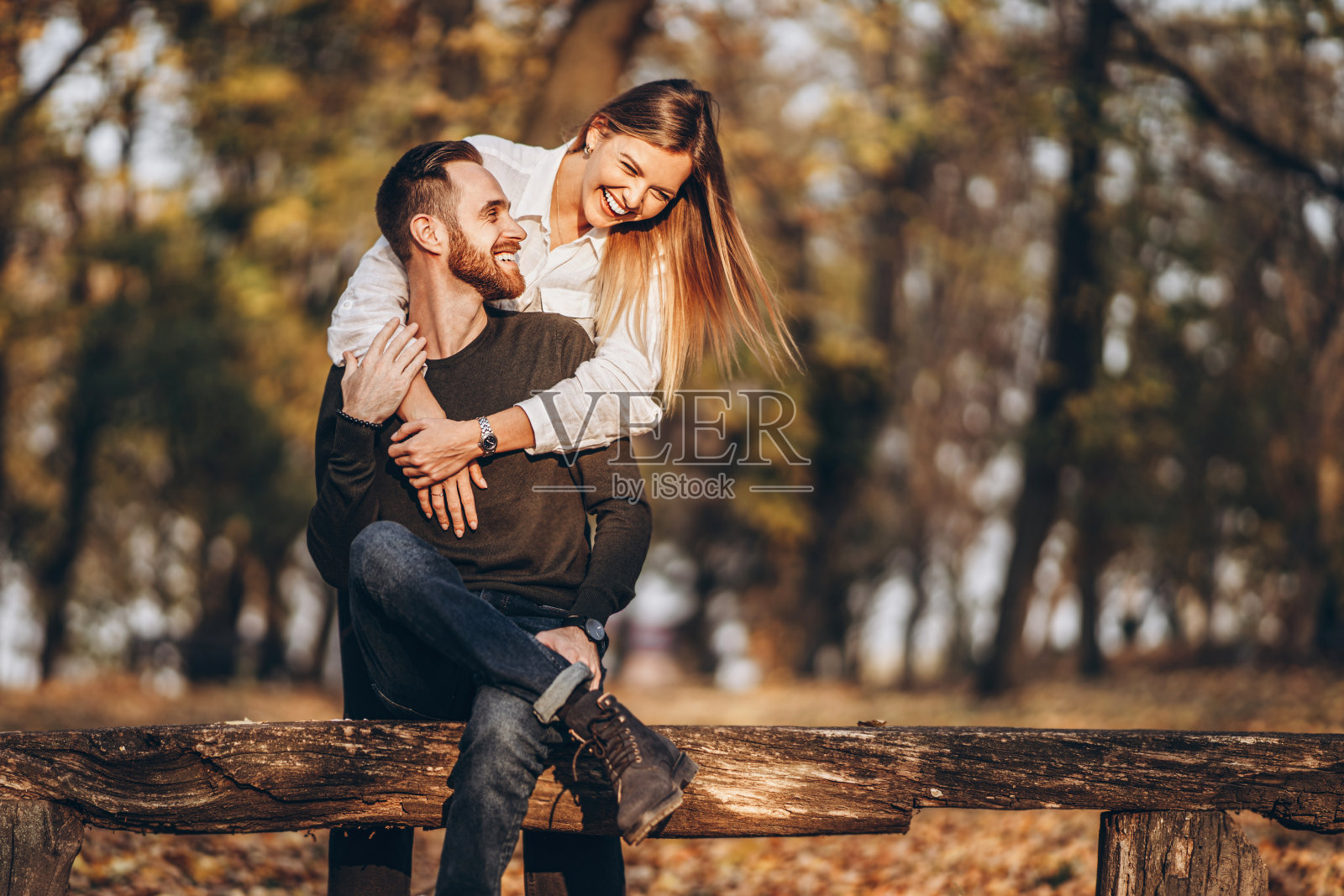 一对年轻的情侣坐在森林里的一张木凳上。照片摄影图片