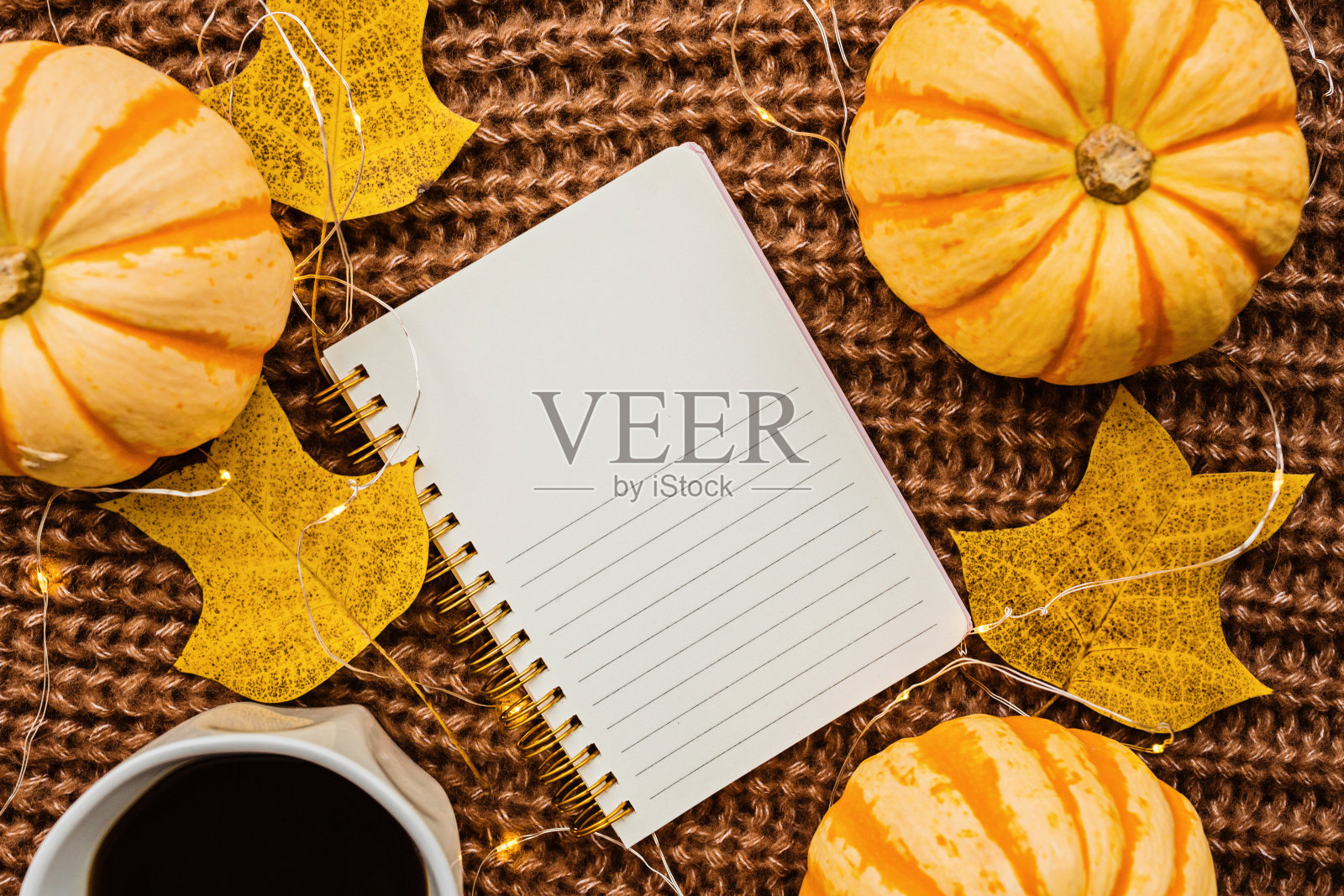 秋天的框架，南瓜，笔记本，咖啡杯和落叶在棕色针织毛衣。秋天、万圣节和感恩节的概念。前视图。为你的文本留出空白照片摄影图片