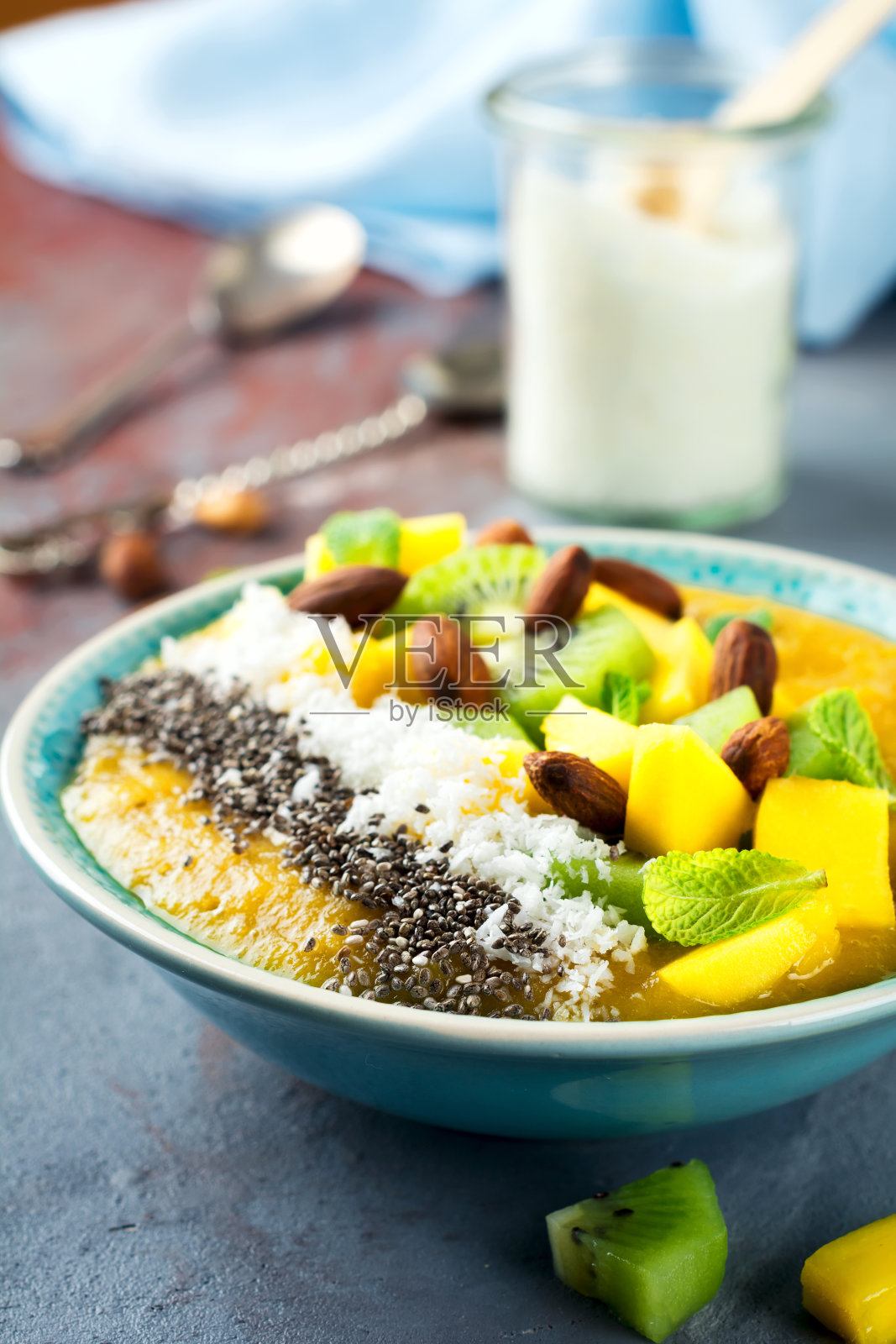芒果冰沙碗，在石头的背景上有猕猴桃、芒果、椰子屑和奇亚籽。有选择性的重点。照片摄影图片