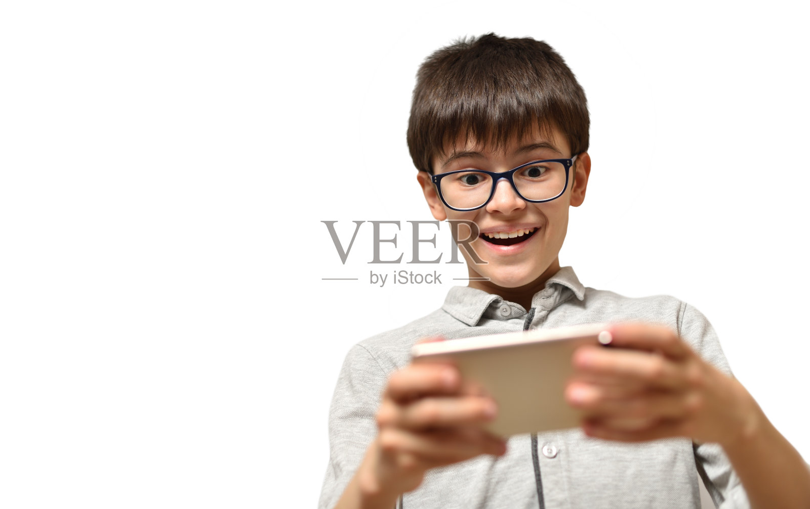一个10-12岁的男孩戴着眼镜在智能手机上玩游戏，在孤立的白色背景上露出惊讶的微笑照片摄影图片