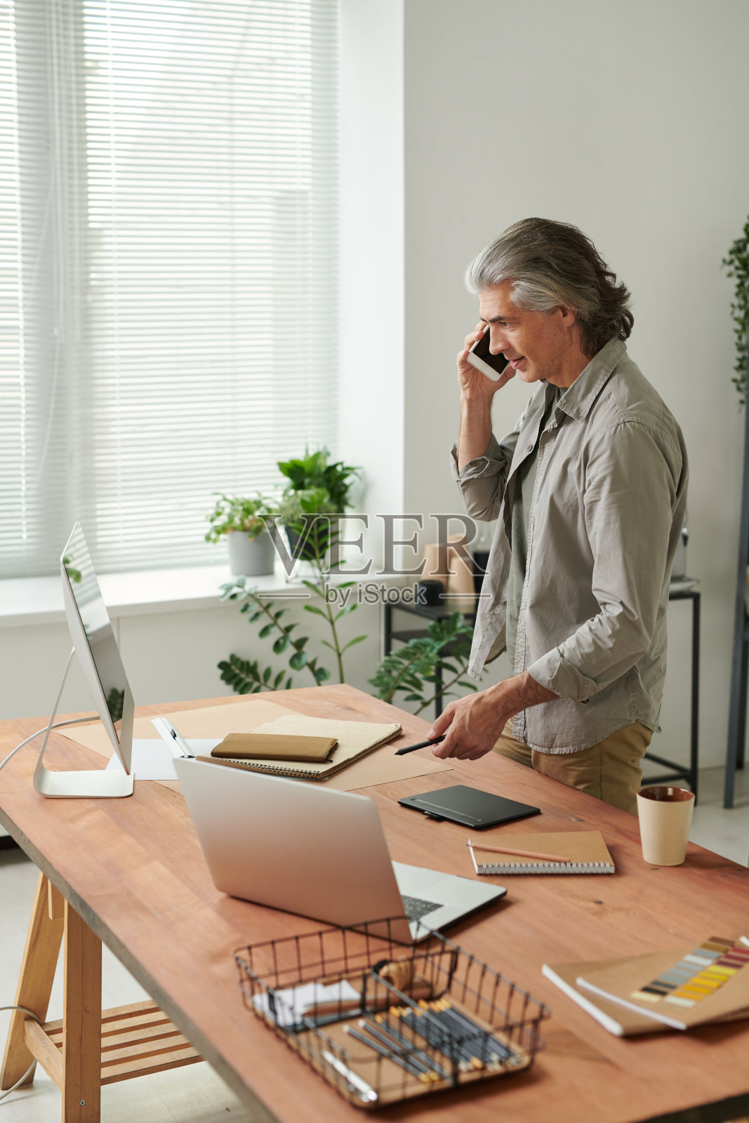 自信成熟的灰发设计师站在办公桌旁打电话，同时向客户解释设计理念照片摄影图片