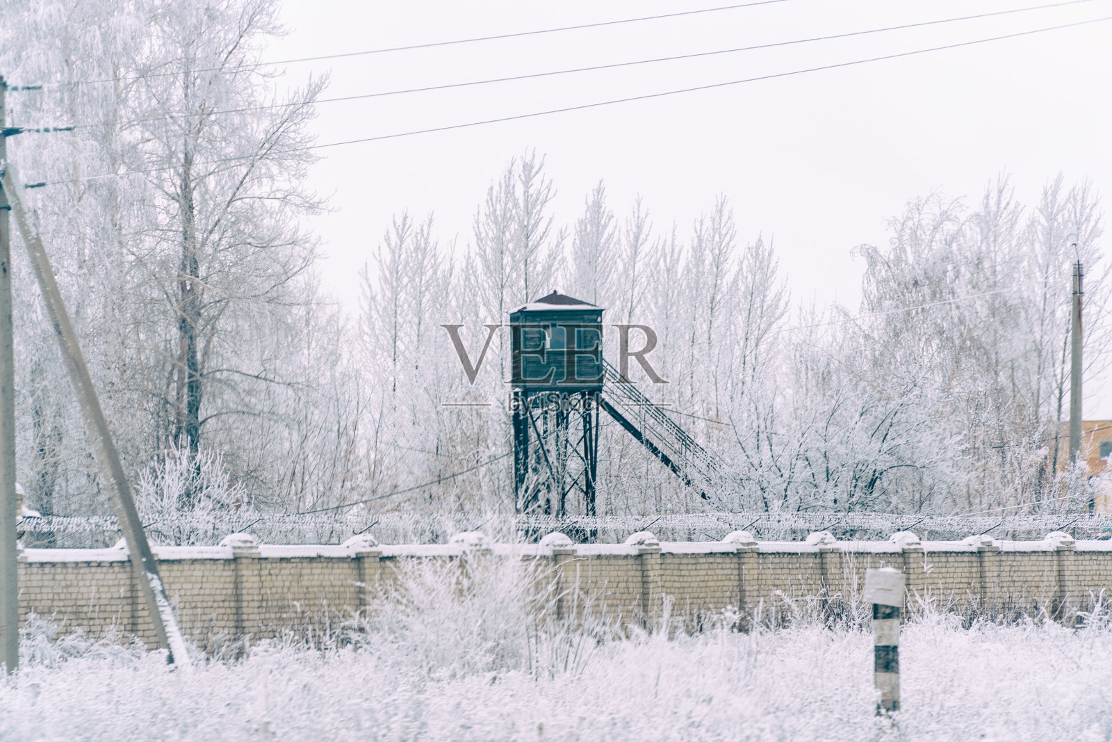 监狱的围墙上有带刺的铁丝网。在冬天的雪地里照片摄影图片