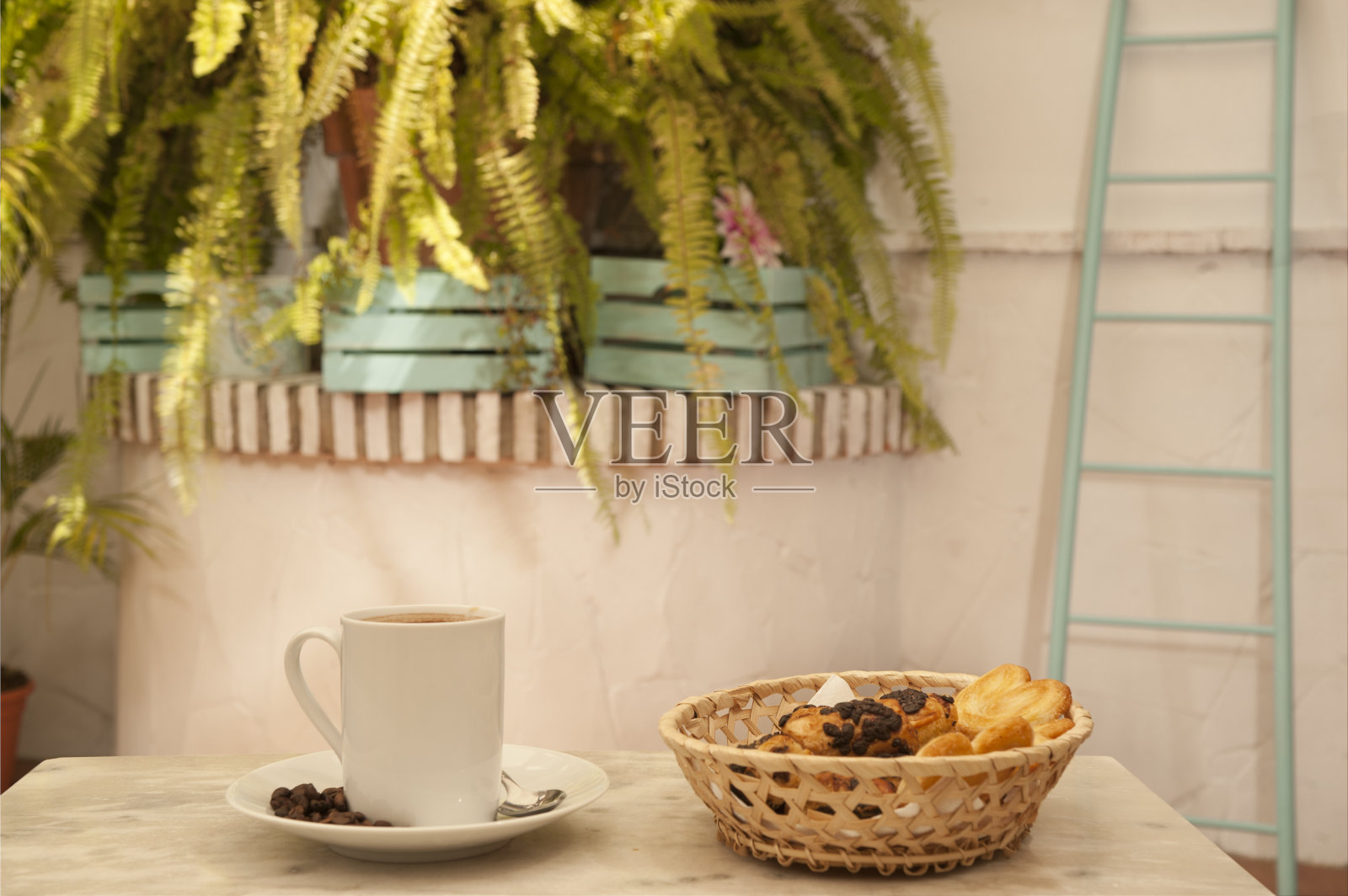大理石桌子上放着一杯咖啡，柳条篮子里放着糕点，地中海房屋的背景是植物照片摄影图片