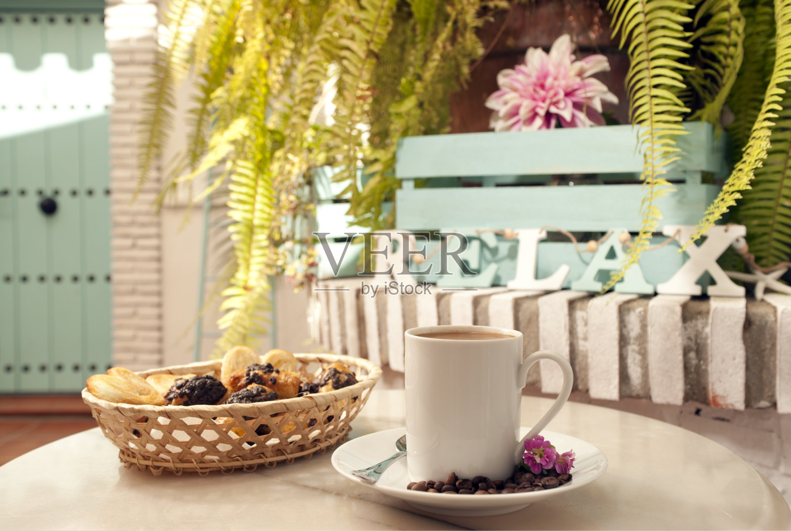 大理石桌子上放着一杯咖啡，柳条篮子里的糕点和装饰植物，背景是地中海的房子照片摄影图片