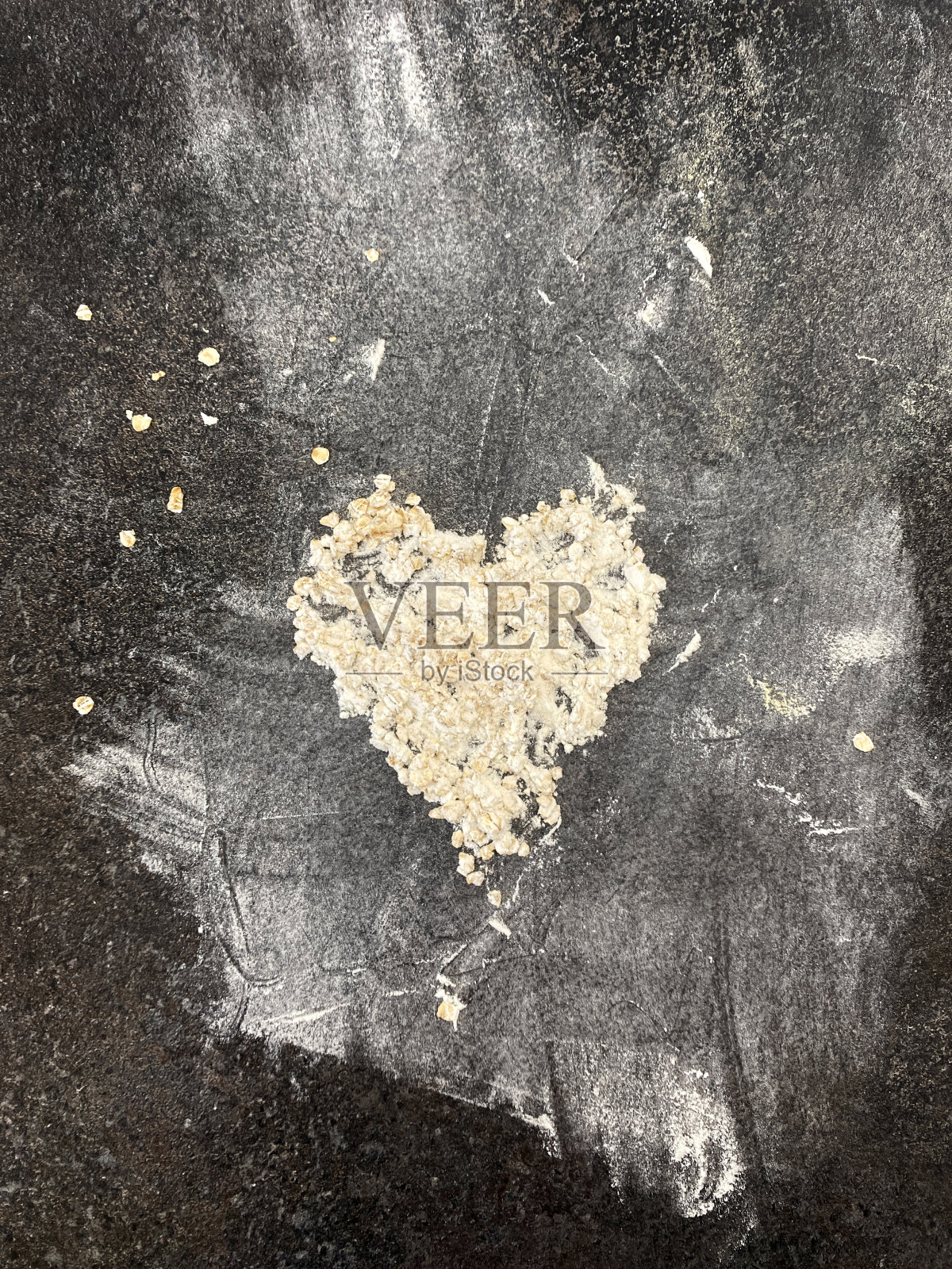 燕麦和燕麦粉在黑色的石头表面上撒成心形。从上面的观点照片摄影图片