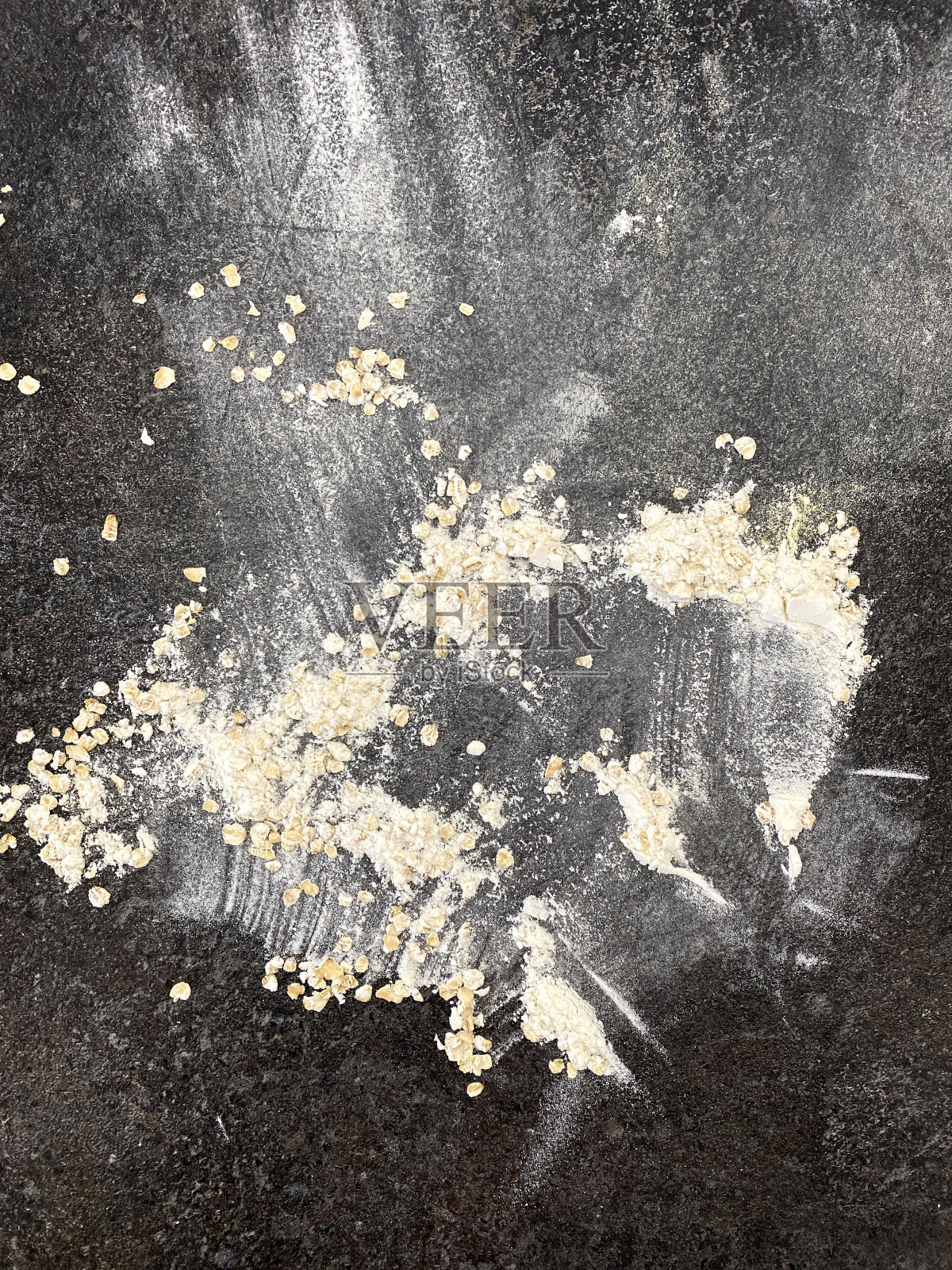 燕麦和燕麦粉在黑色的石头表面上撒成心形。从上面的观点照片摄影图片